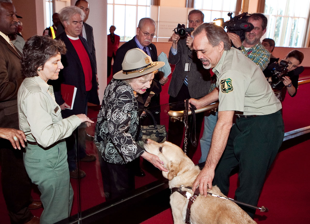 Betty White (center) wearing a park ranger hat and petting a yellow dog