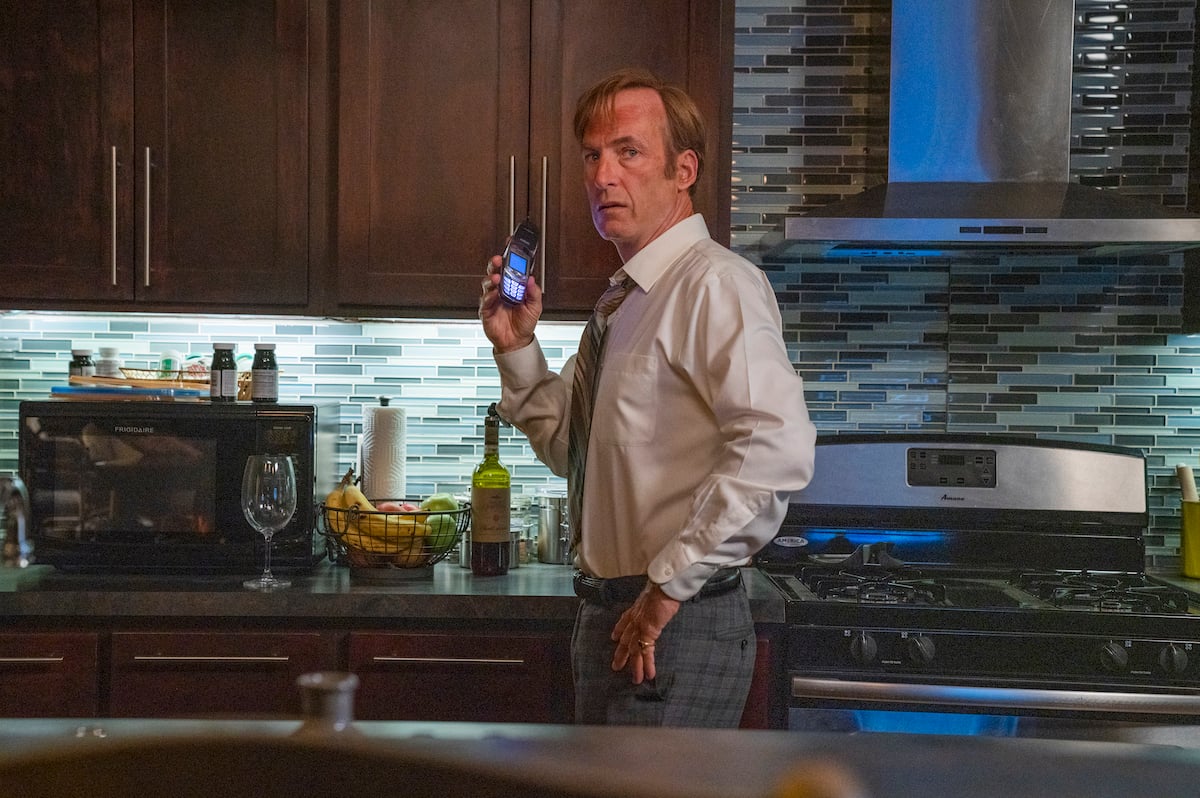 Bob Odenkirk as Saul Goodman wearing a white shirt and gray pants with a phone in his hand in a scene from the AMC series 'Better Call Saul'