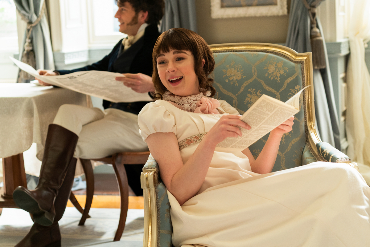 Jonathan Bailey as Anthony Bridgerton and Claudia Jesse as Eloise Bridgerton. Eloise reads a pamphlet and smiles. Anthony sits behind her. 