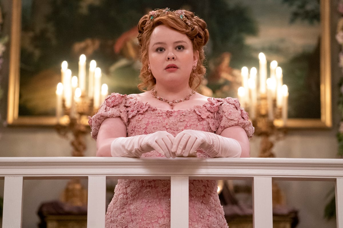 Nicola Coughlan as Penelope Featherington in Bridgerton Season 2. Penelope wears a pink dress and leans against a railing.