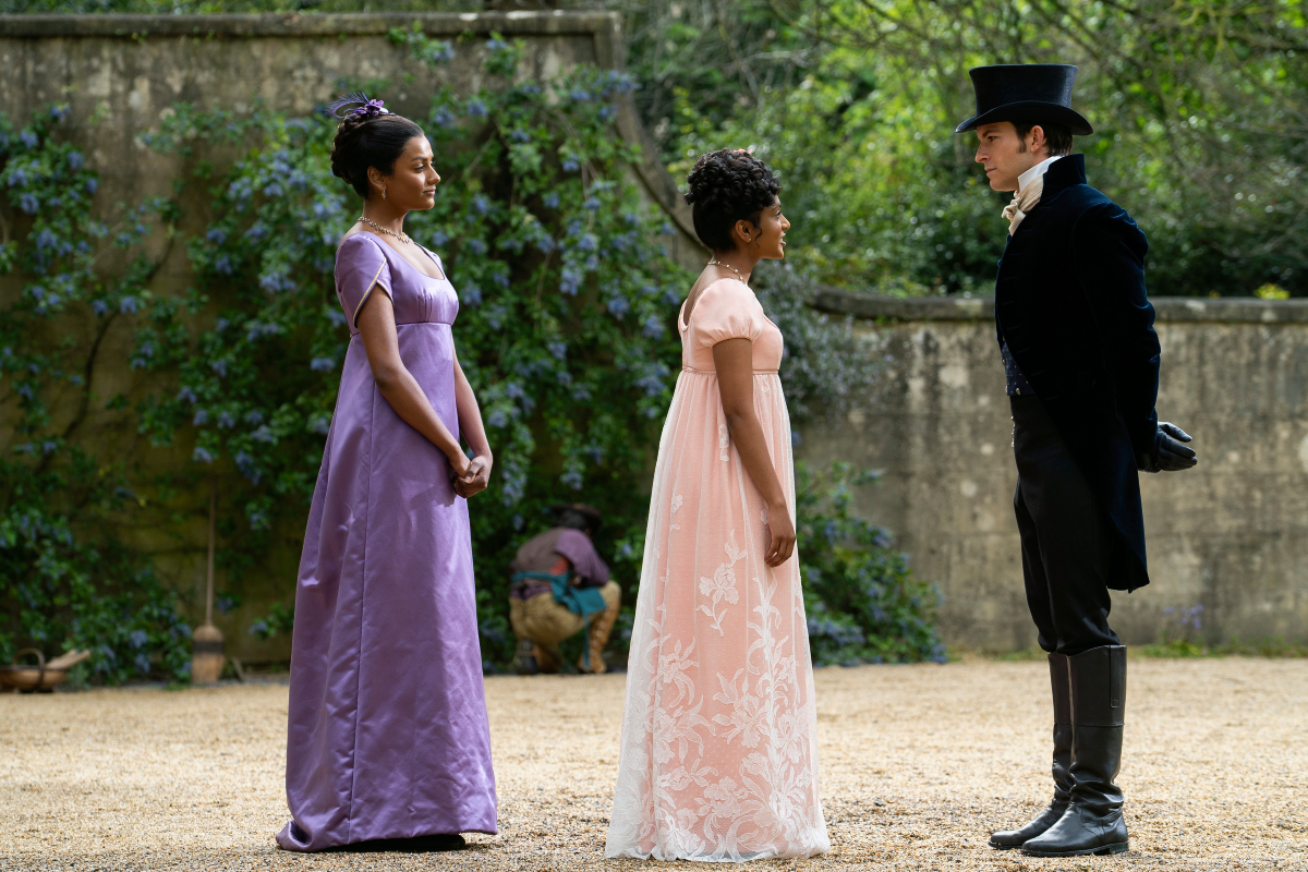 Simone Ashley as Kate Sharma, Charithra Chandran as Edwina Sharma, and Jonathan Bailey as Anthony Bridgerton in Bridgerton Season 2. Edwina faces Anthony. Kate stands behind her.