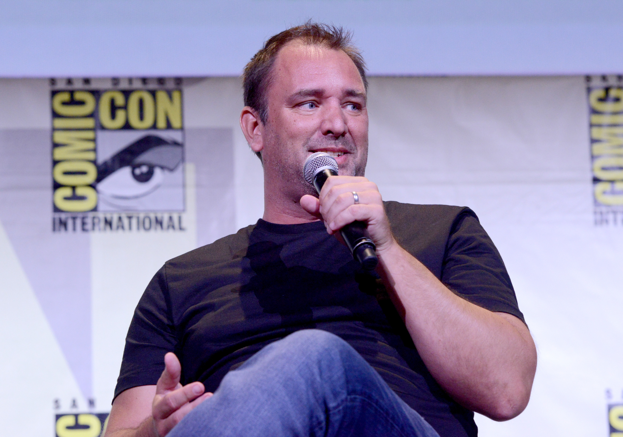 'Cannibal! The Musical' movie director Trey Parker wearing a crew neck shirt and blue jeans holding a microphone in front of the Comic Con logo