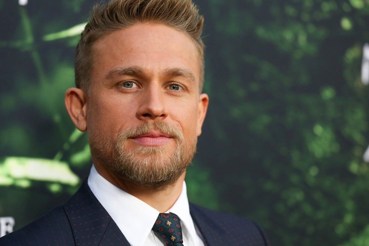Charlie Hunnam smirking while wearing a suit.