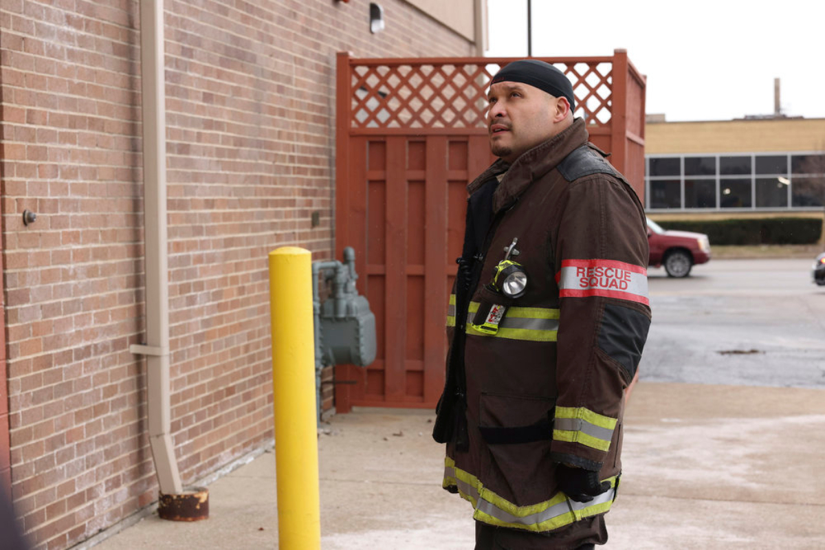 Joe Minoso as Joe Cruz in Chicago Fire Season 10. Cruz stands outside a building looking up. 