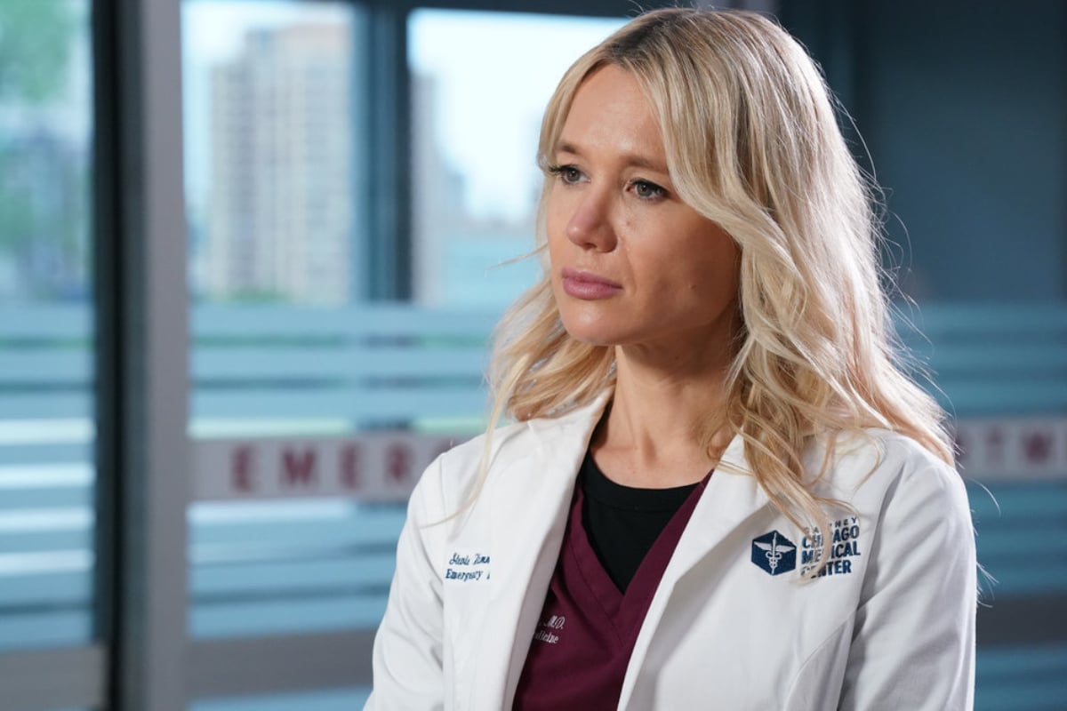 Kristen Hager as Dr. Stevie Hammer in Chicago Med Season 7. Hammer wears maroon scrubs and a white doctor's coat.