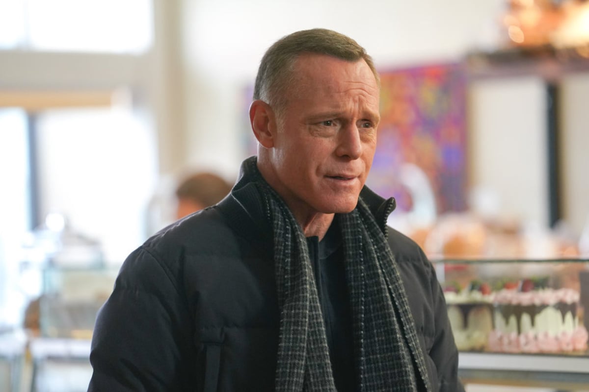 Jason Beghe as Hank Voight in Chicago P.D. Season 9. Voight stands in a bakery wearing a coat and scarf. 