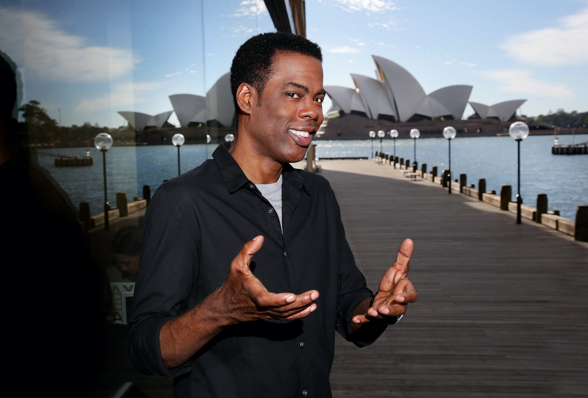 Chris Rock pose avec ses mains et l'Opéra de Sydney en arrière-plan