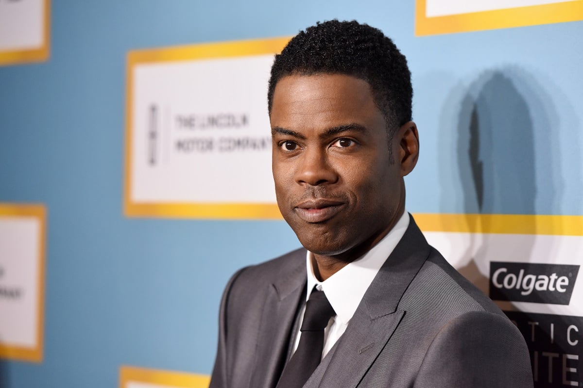 Chris Rock smirking while wearing a grey