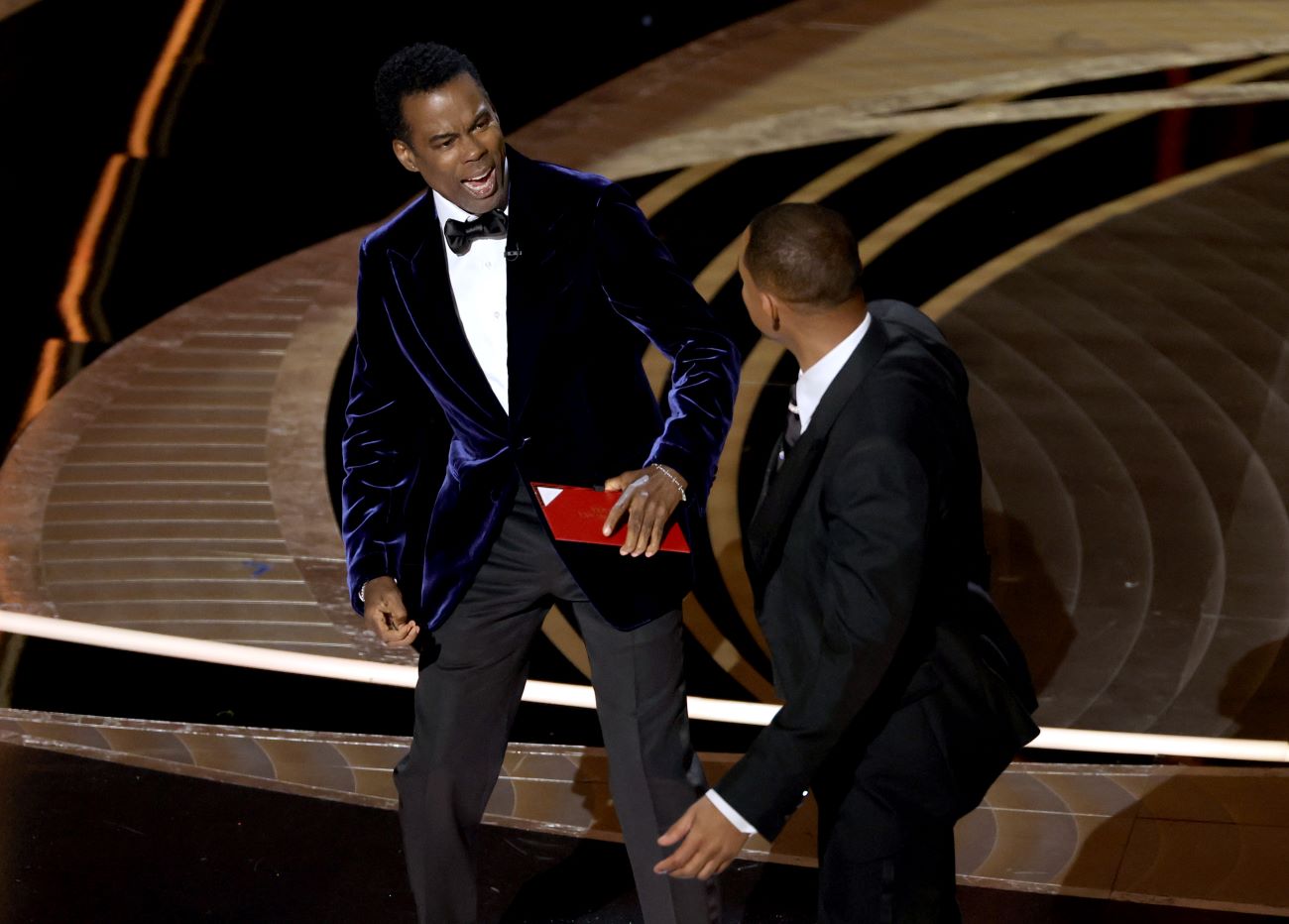 Chris Rock and Will Smith onstage at the Oscars. Chris Rock reacts to Will Smith hitting him.