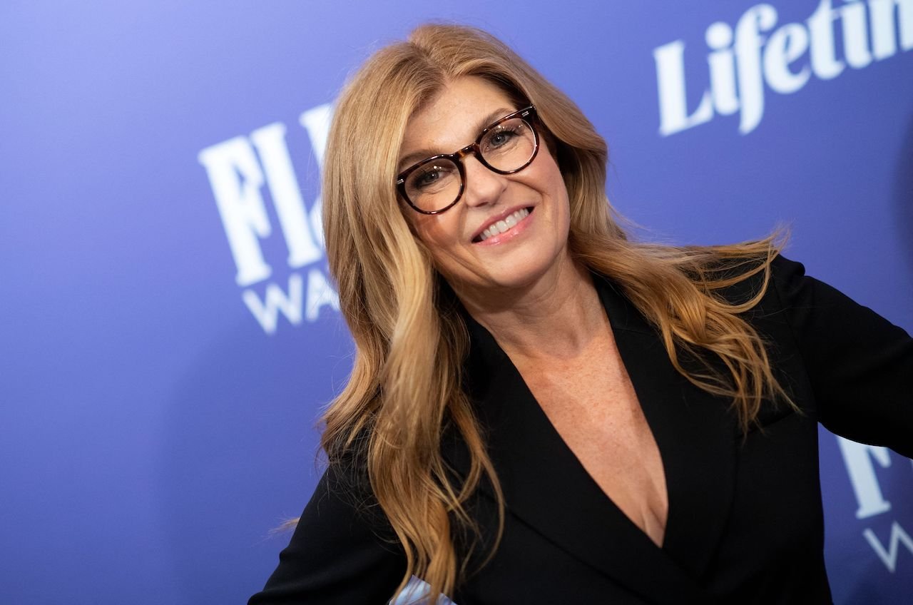 Connie Britton smiles for a picture in a black top and glasses