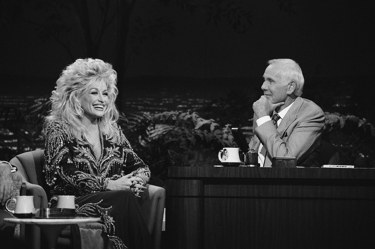 Black and white photo of Dolly Parton seated next to Johnny Carson at 'The Tonight Show' desk in 1990