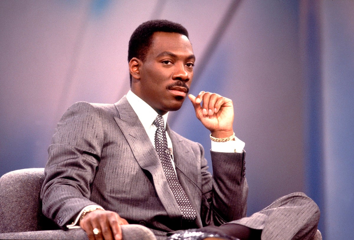 Eddie Murphy sitting down smirking while wearing a suit.