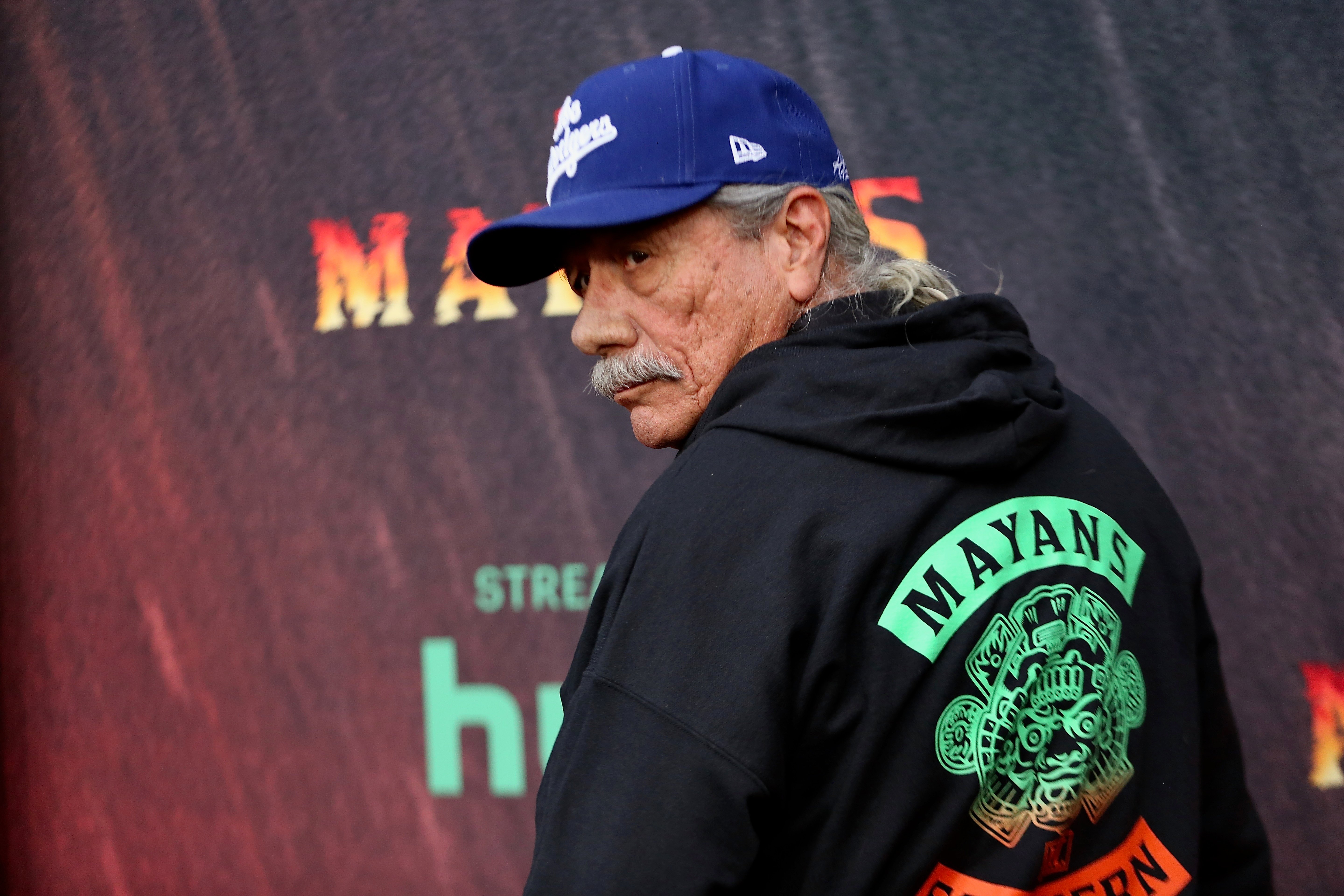 Edward James Olmos at the premiere for Mayans MC Season 4 wearing a Mayans MC hoodie and baseball cap.