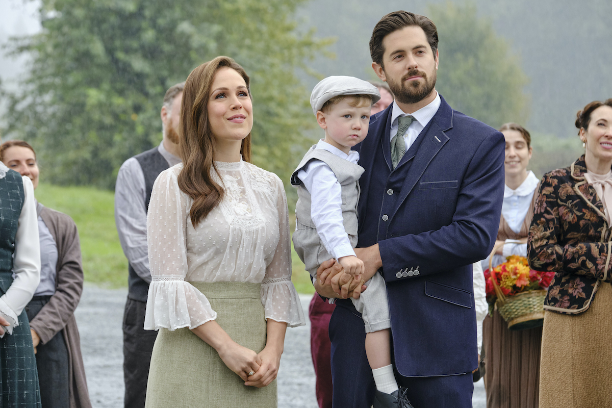 Elizabeth standing next to Lucas, who is holding Little Jack, in 'When Calls the Heart' Season 9 Episode 8