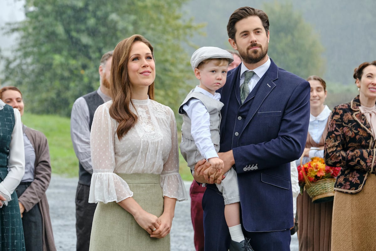 Elizabeth standing next to Lucas, who is holding Little Jack, in 'When Calls the Heart' Season 9 Episode 8