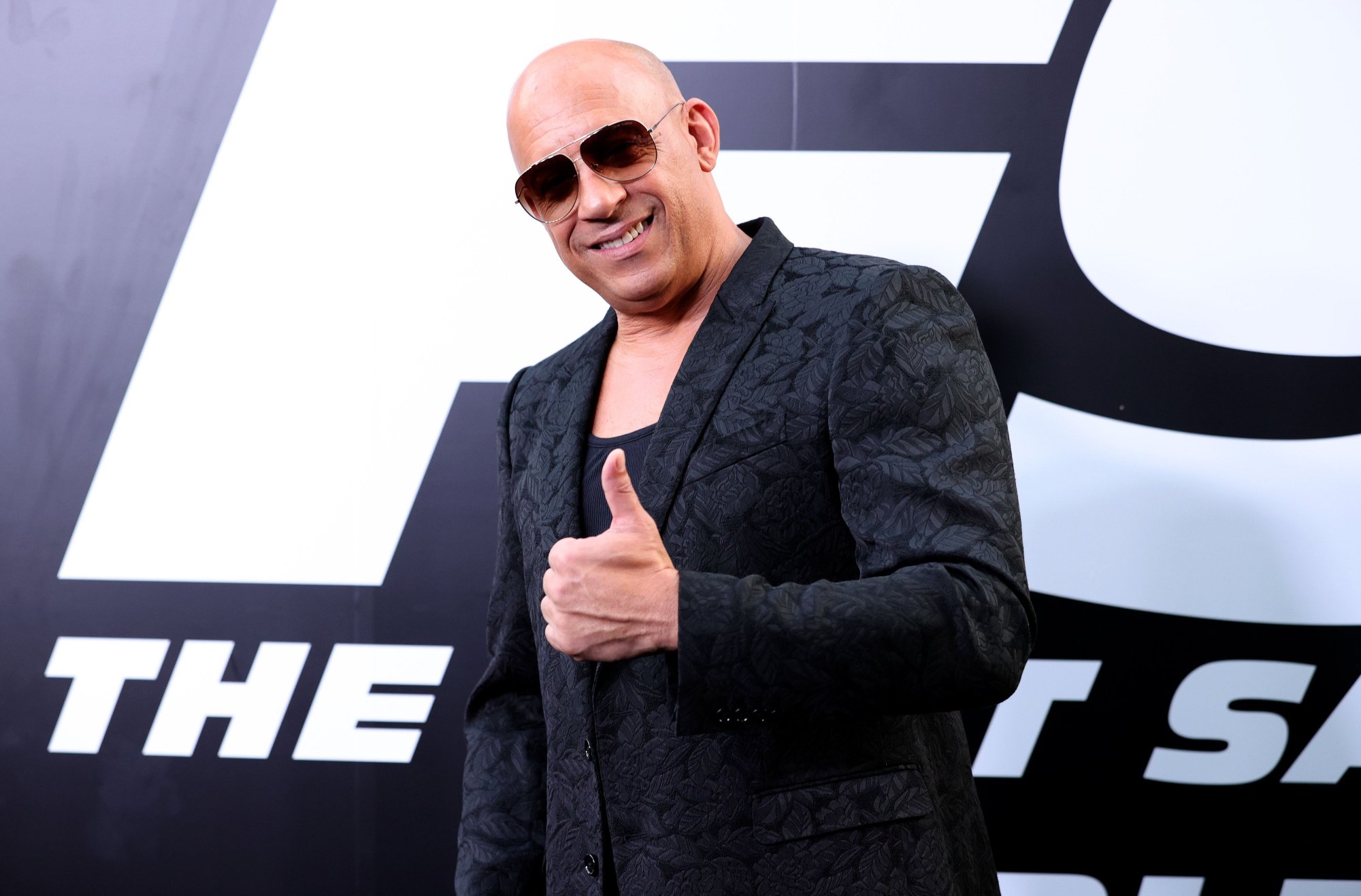 'Fast & Furious' actor Vin Diesel standing in front of 'F9' step and repeat with a thumb up and wearing sunglasses