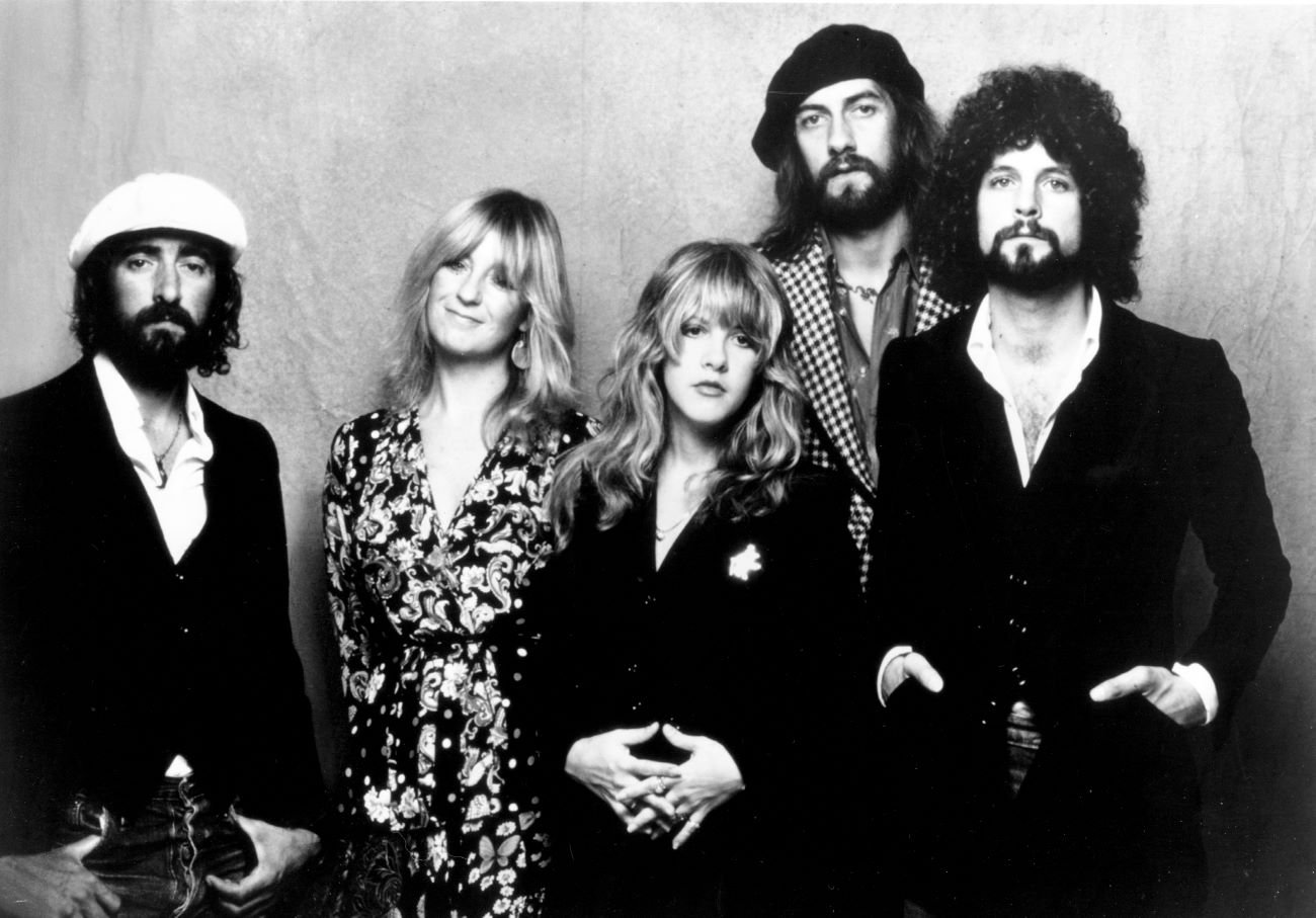 A black and white photo of John McVie, Christine McVie, Stevie Nicks, Mick Fleetwood, and Lindsey Buckingham standing together.