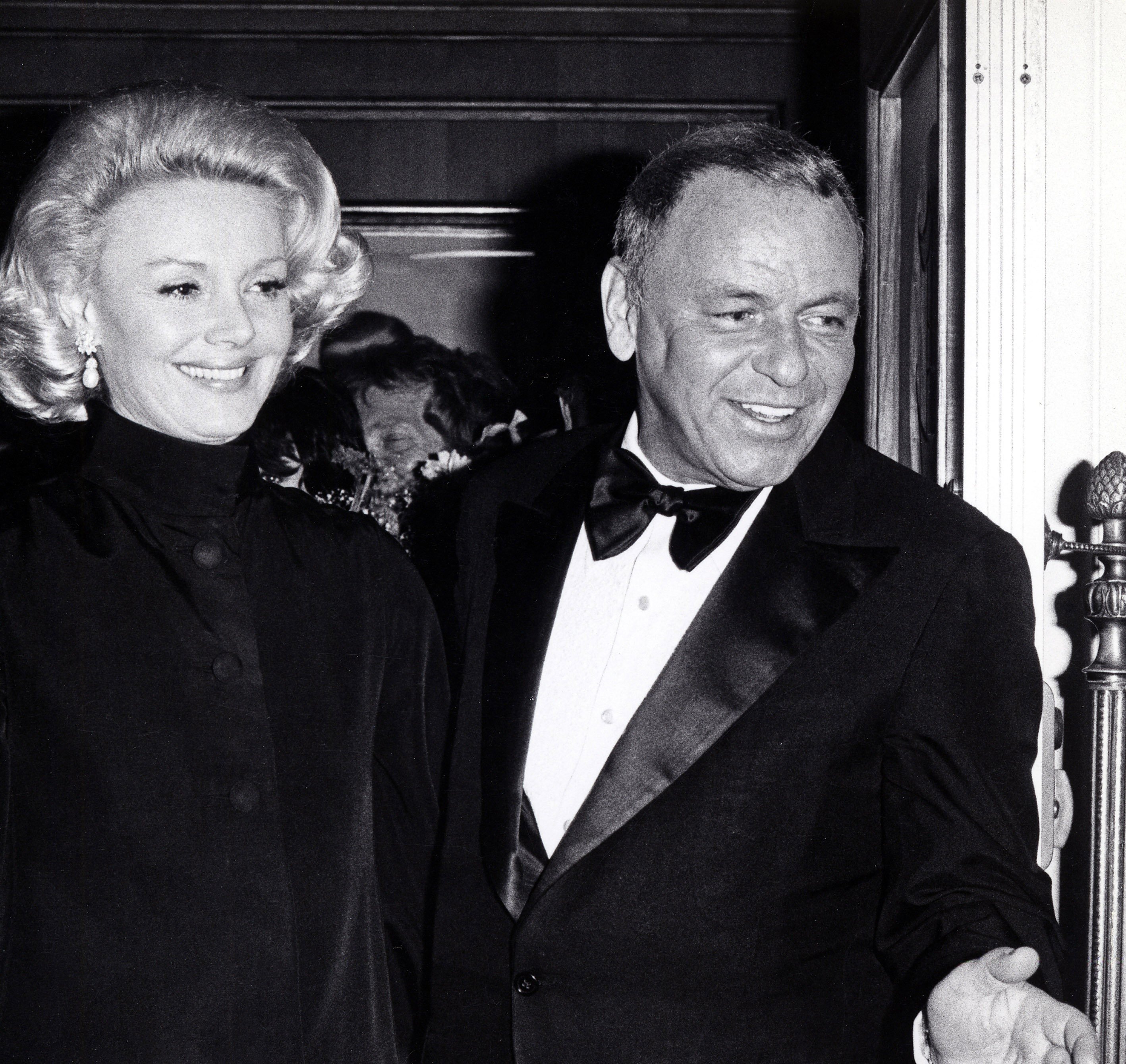A black and white photo of Frank Sinatra and his wife Barbara Sinatra leaving the Oscars. They both smile.