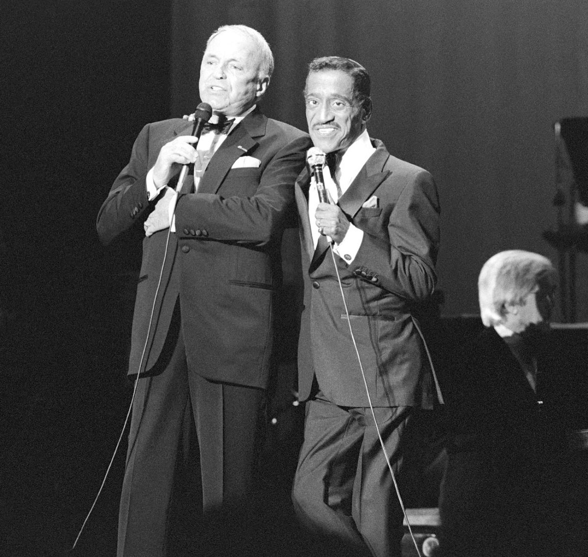 A black and white photo of Frank Sinatra and Sammy Davis Jr. wearing tuxedos and holding microphones.