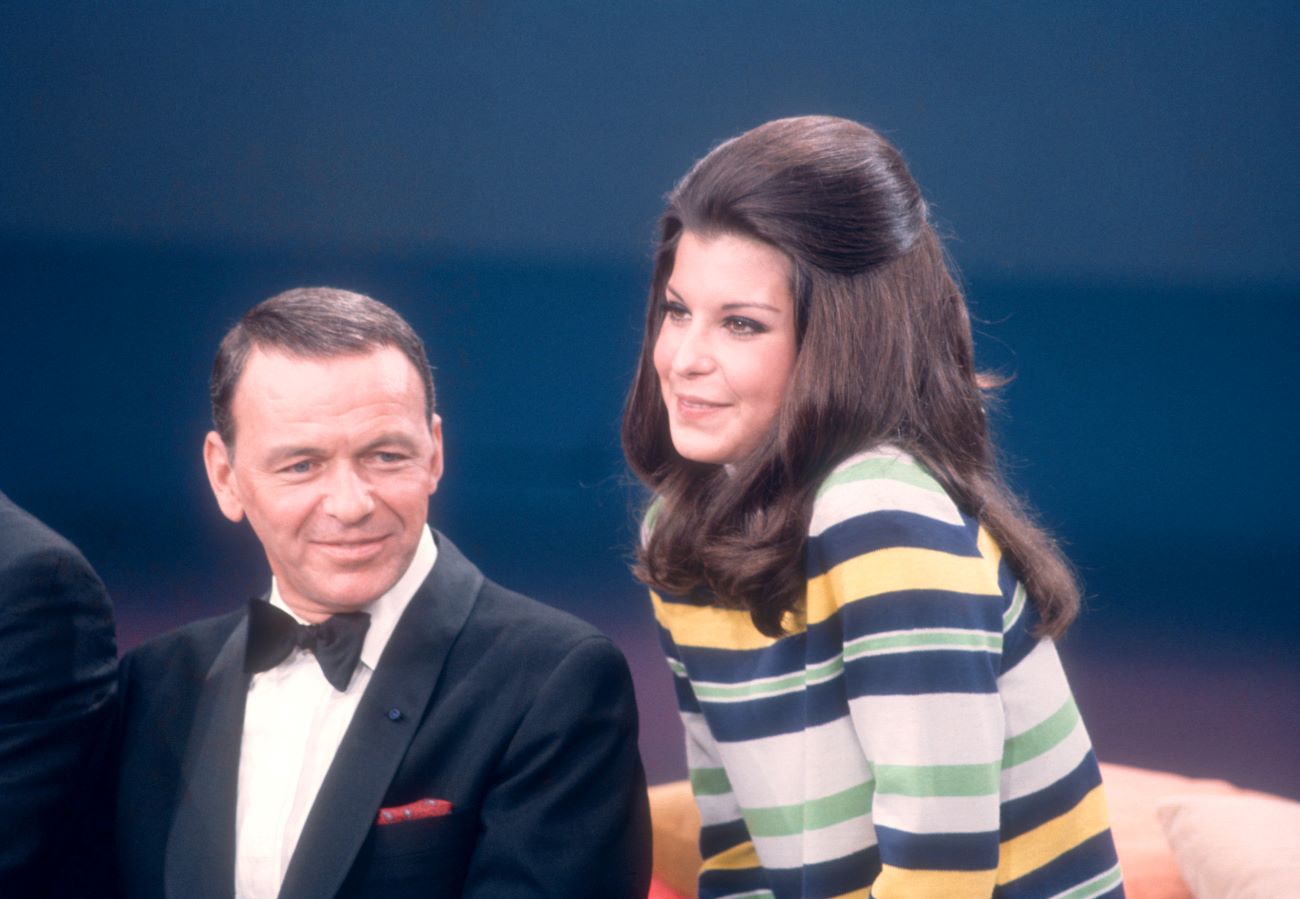 Frank Sinatra sits wearing a tuxedo. His daughter Tina Sinatra wears a striped shirt next to him.
