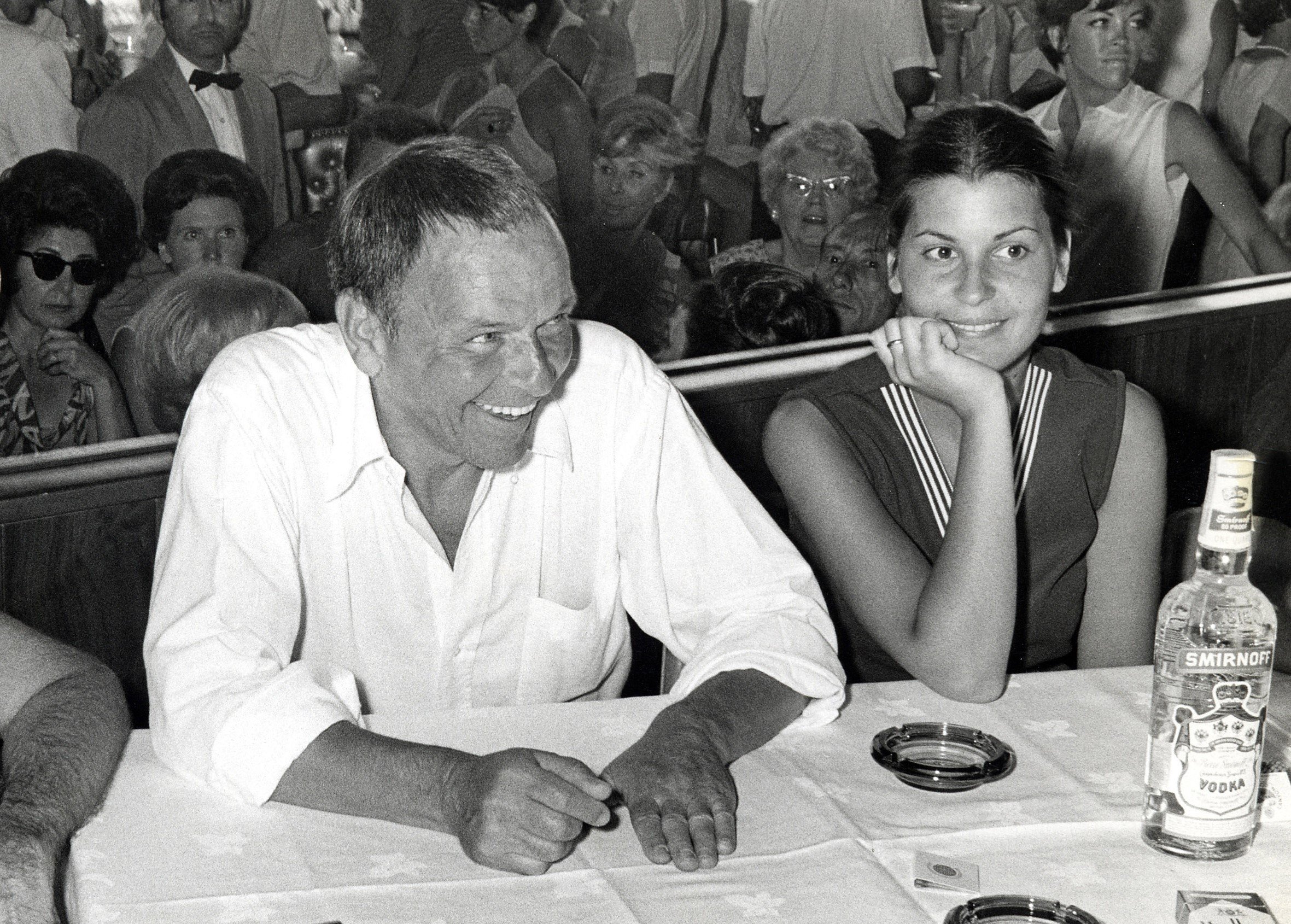 A black and white picture of Frank Sinatra and his daughter Tina Sinatra sitting at a table with a group of people behind them.