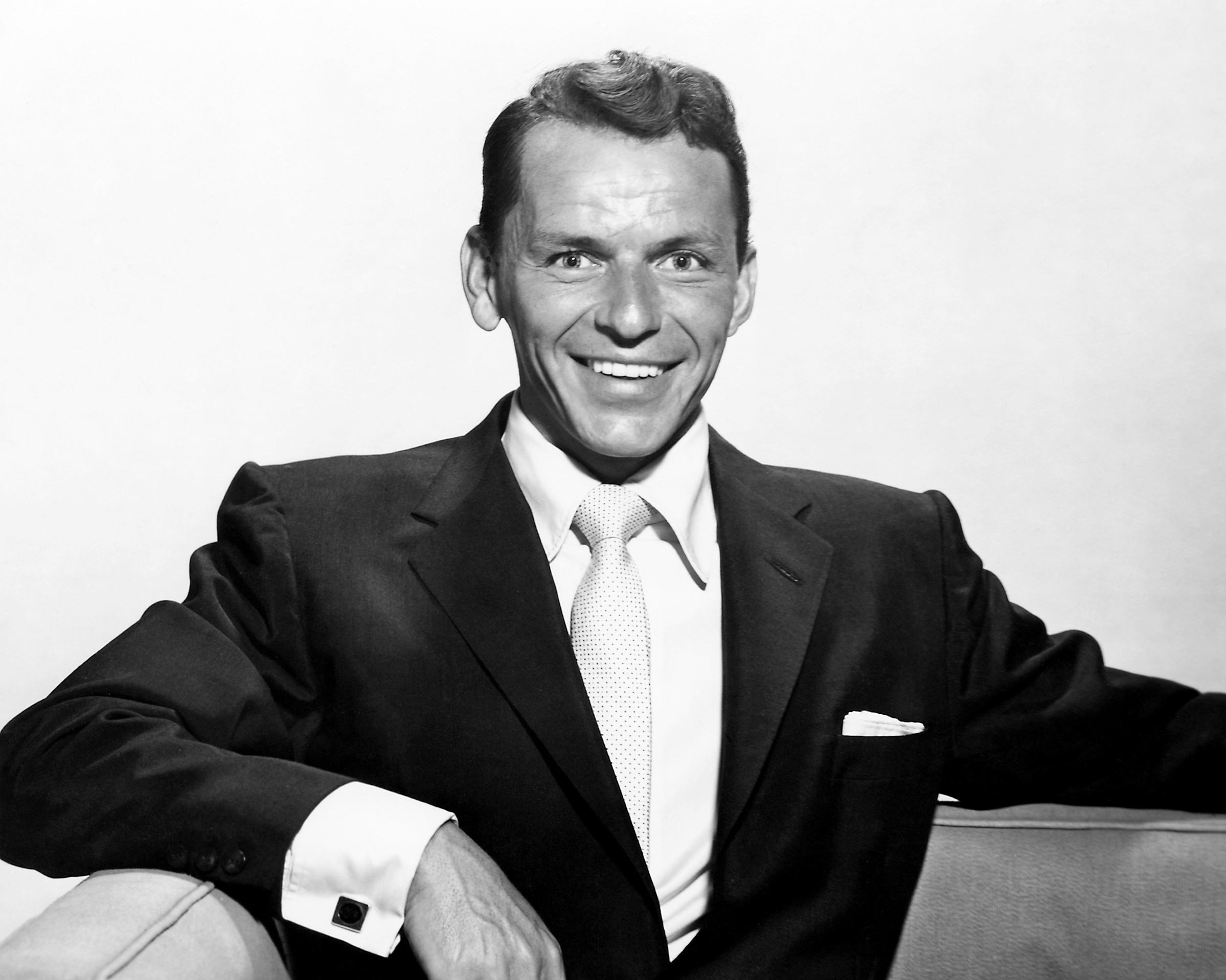 A black and white photo of Frank Sinatra sitting and wearing a suit.