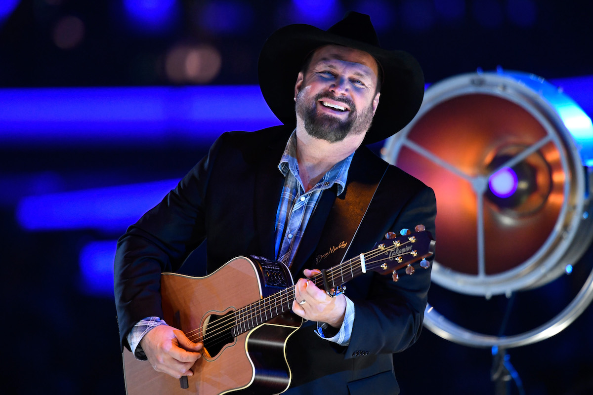 Garth Brooks smiles and plays guitar on stage.