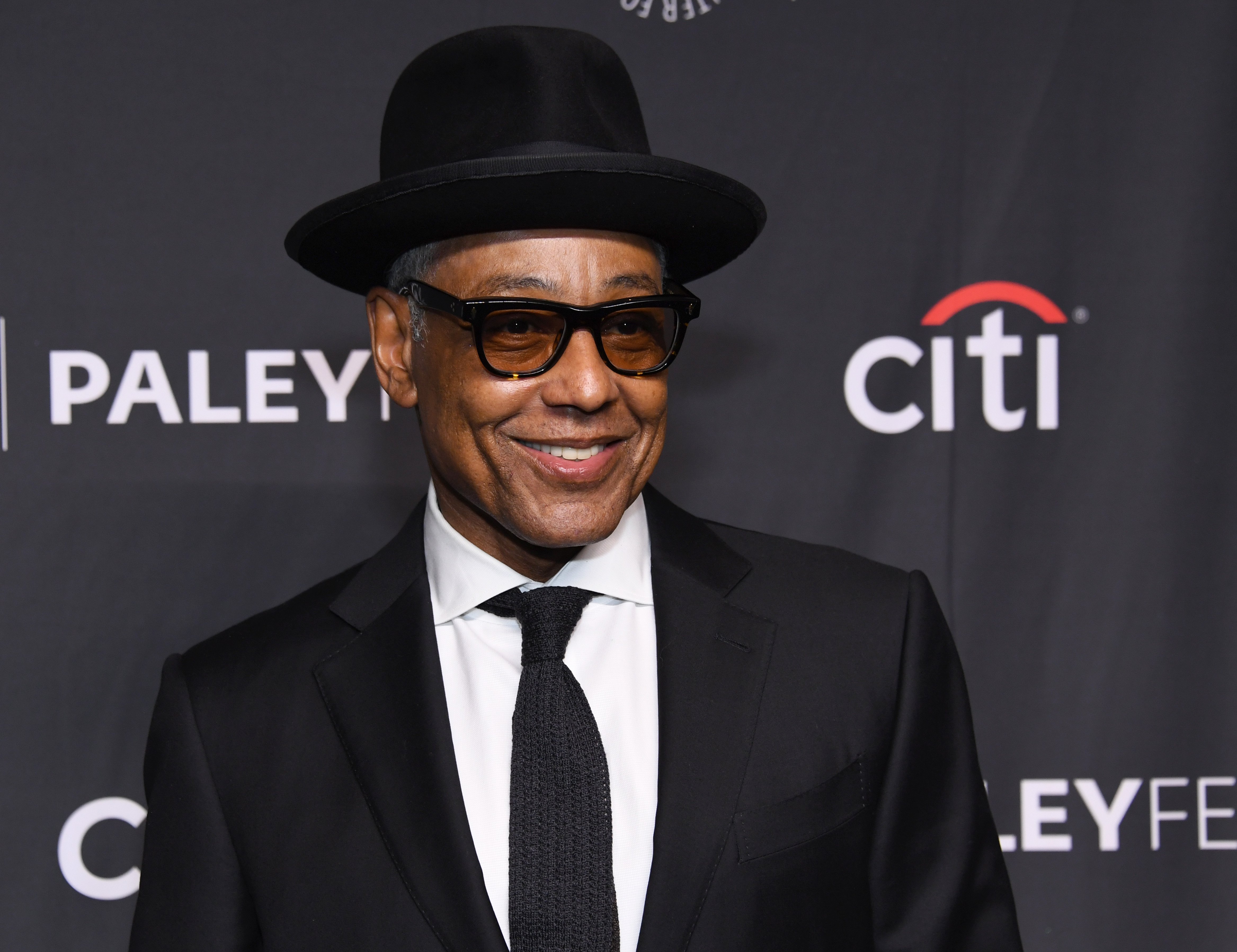 Giancarlo Esposito from Better Call Saul wearing a suit, black hat, and glasses. 