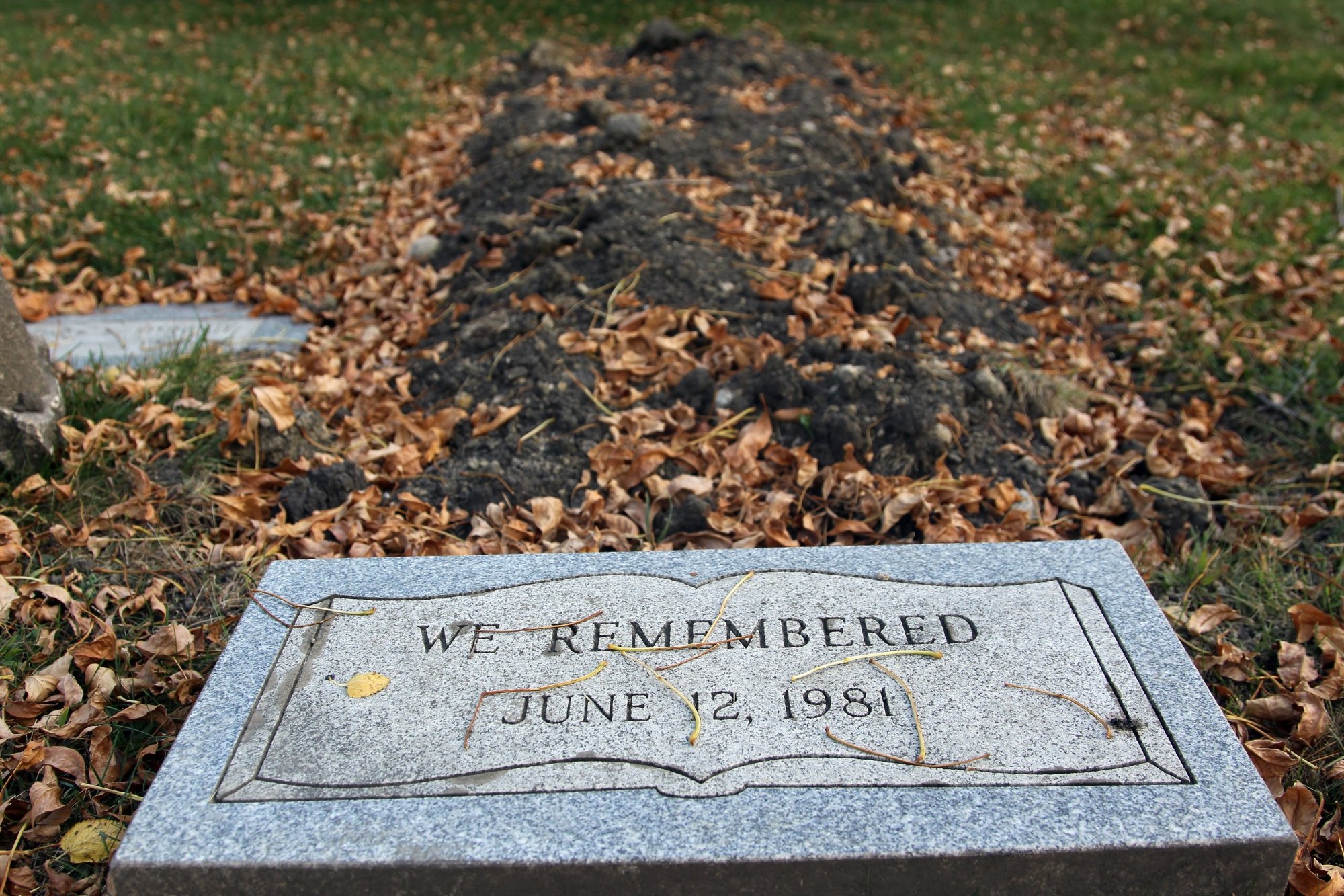 Grave of unidentified victim of John Wayne Gacy with leaves on the ground