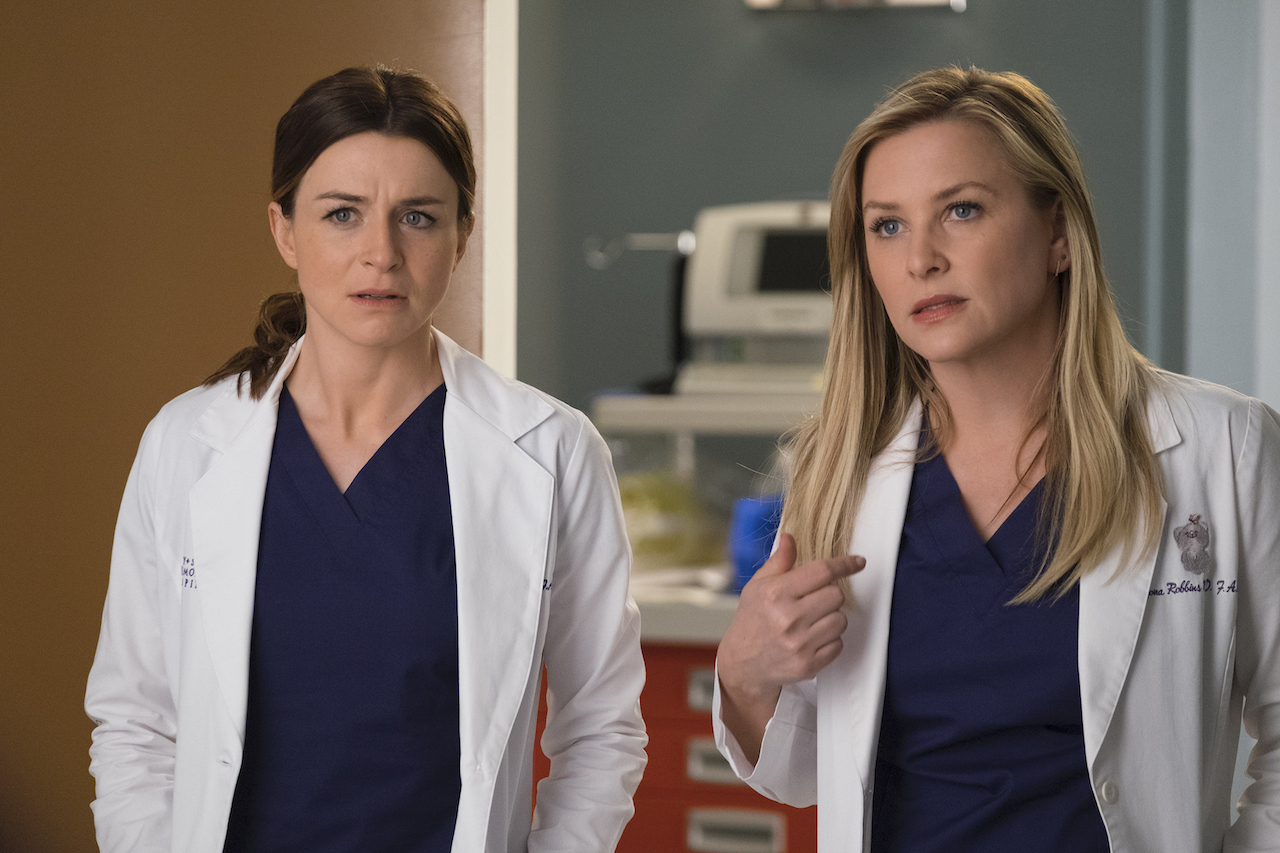 Caterina Scorsone as Amelia Shepherd and Jessica Capshaw as Arizona Robbins talk to someone in scrubs and white coats in 'Grey's Anatomy'.