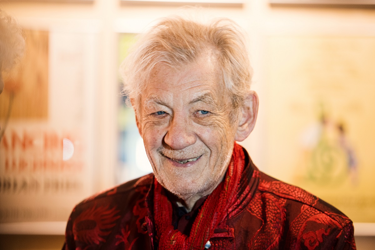 Ian McKellen smiling while wearing a red jacket.