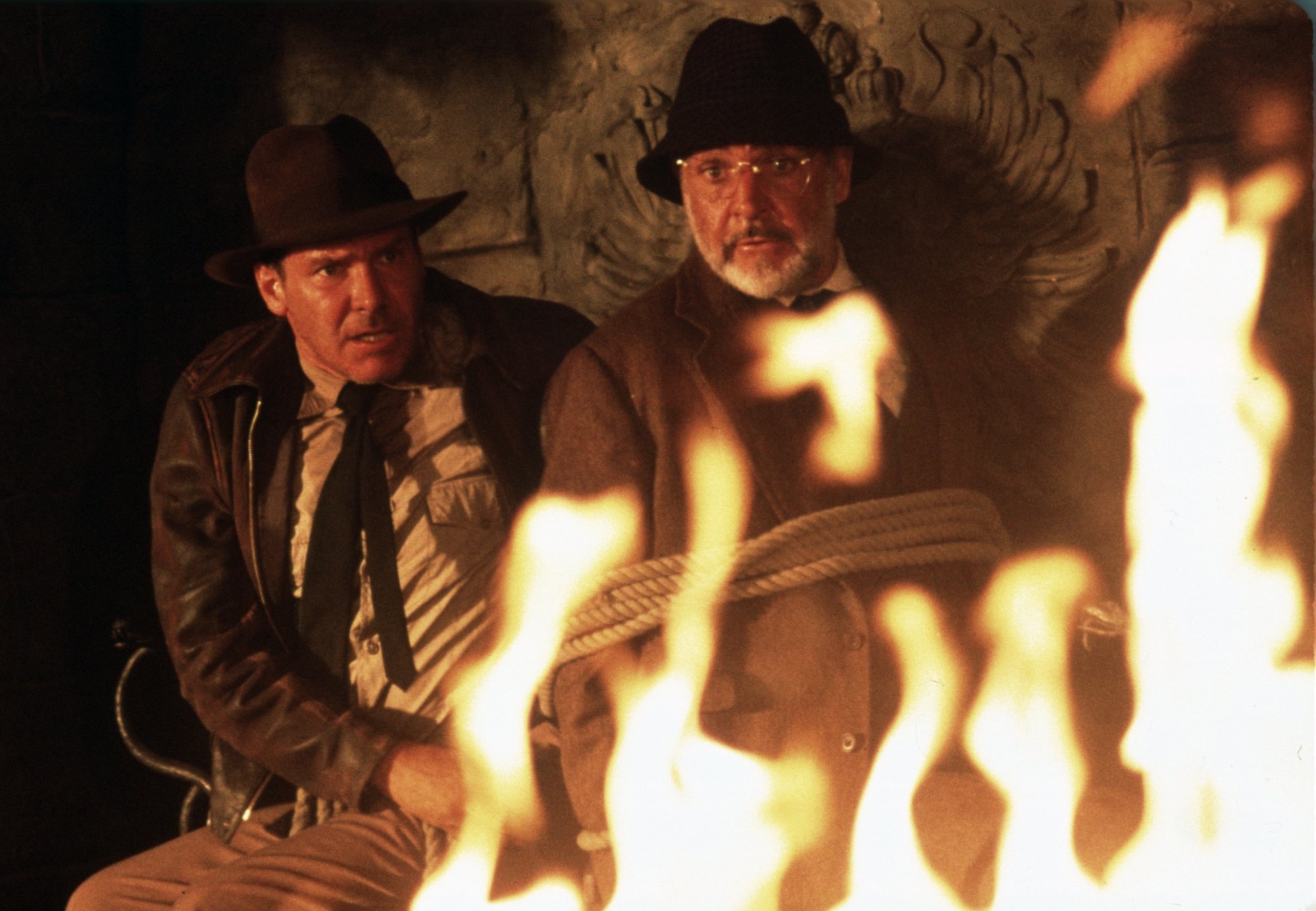 'Indiana Jones and the Last Crusade' Harrison Ford as Indiana Jones and Sean Connery as Henry Jones, Sr. looking panicked in front of a fire with Connery tied up in ropes