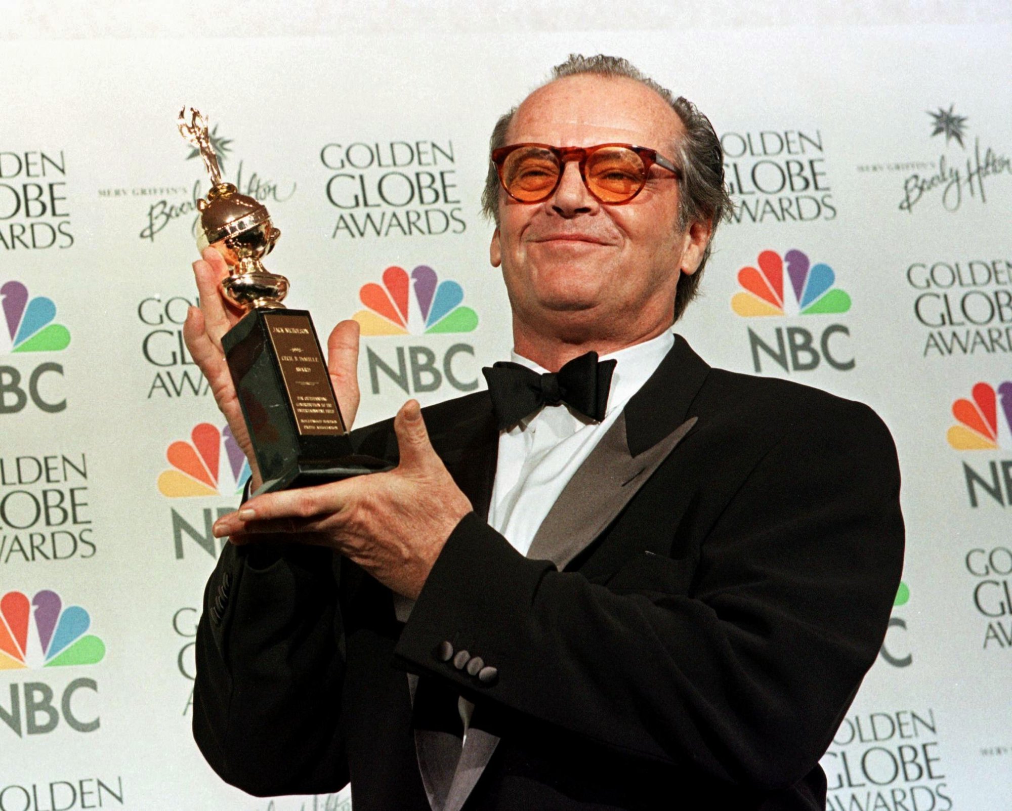 Jack Nicholson with his Cecil B. DeMille Award at the Golden Globes after talking about the New York Yankees in speech in a tuxedo in front of a step and repeat