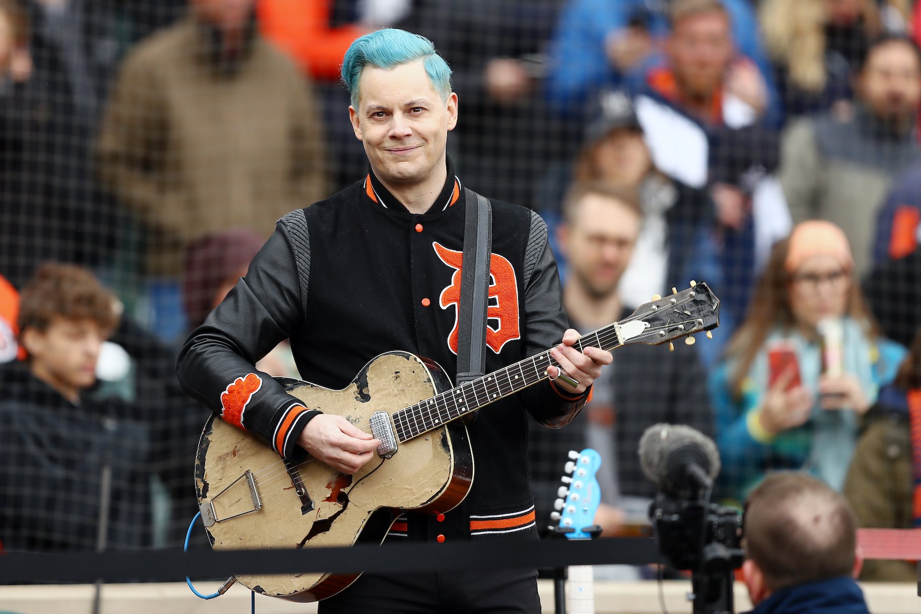 Jack White holding a guitar and smiling at a sports game