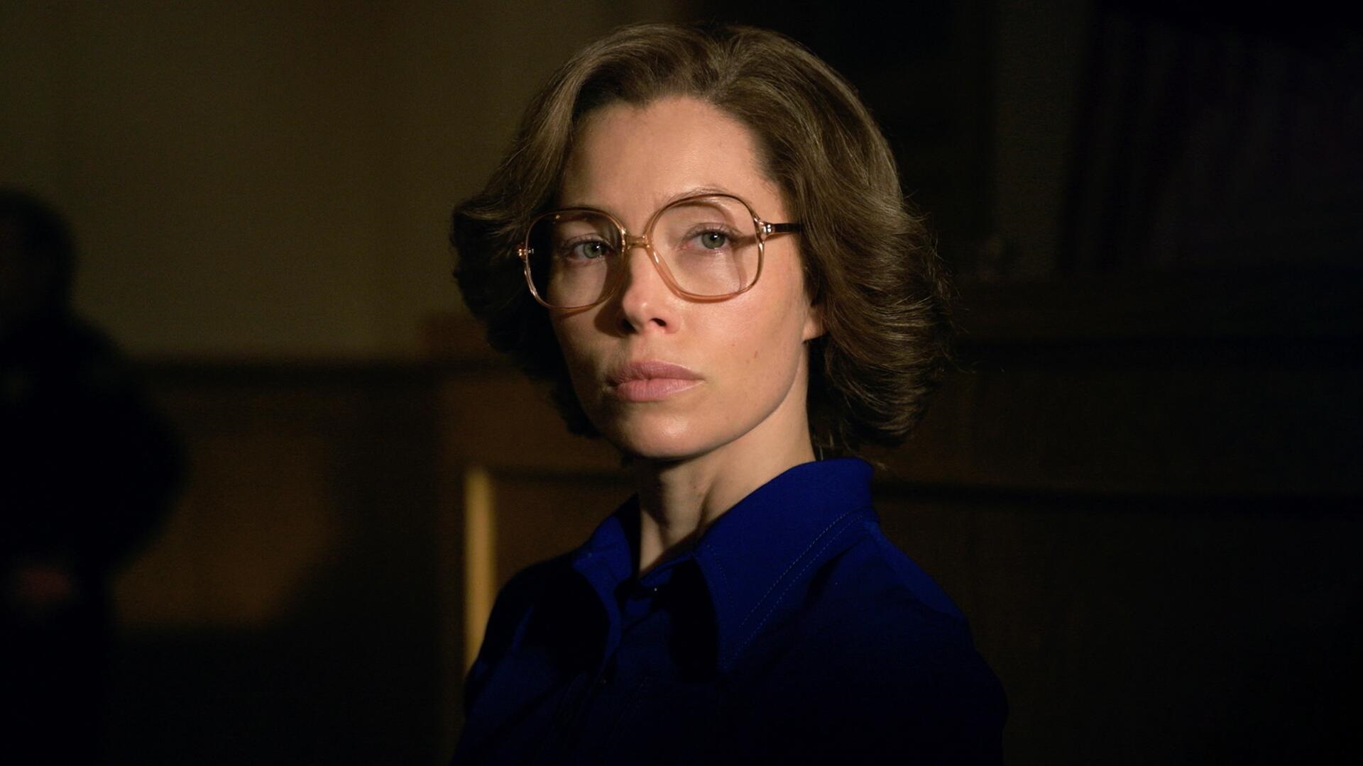 Jessica Biel wearing large square-rimmed glasses looking at the camera portays Candy Montgomery in the Hulu true crime 'Candy'