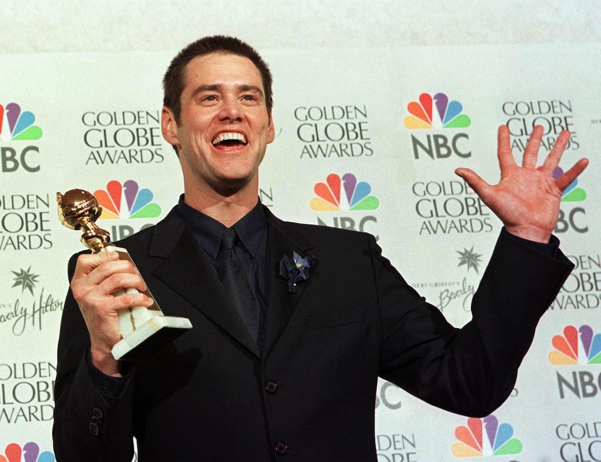 Jim Carrey wears a black suit and holds up his Golden Globe Award