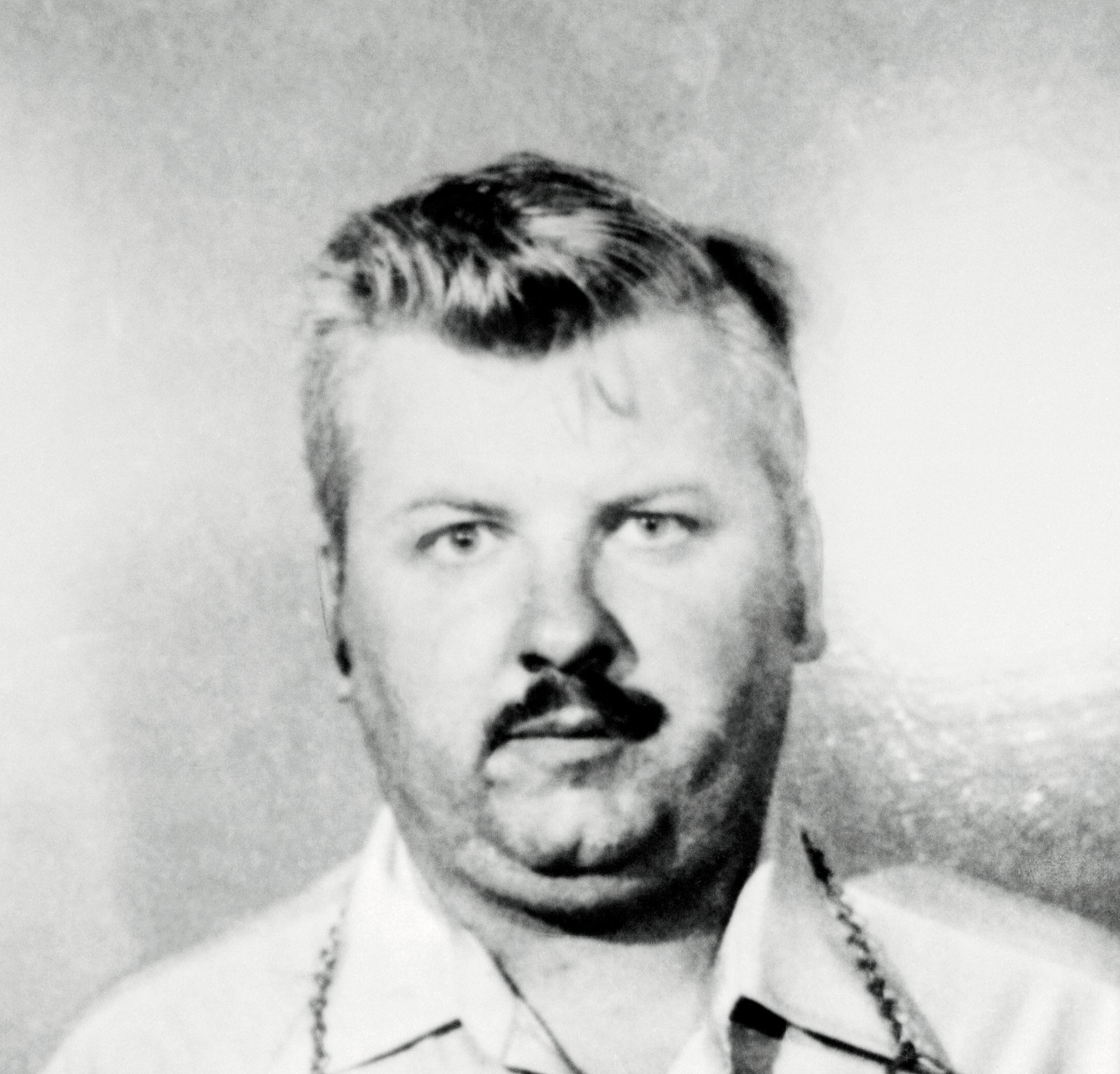 John Wayne Gacy after killing dozens of victims in black-and-white staring directly into the camera with a collared shirt