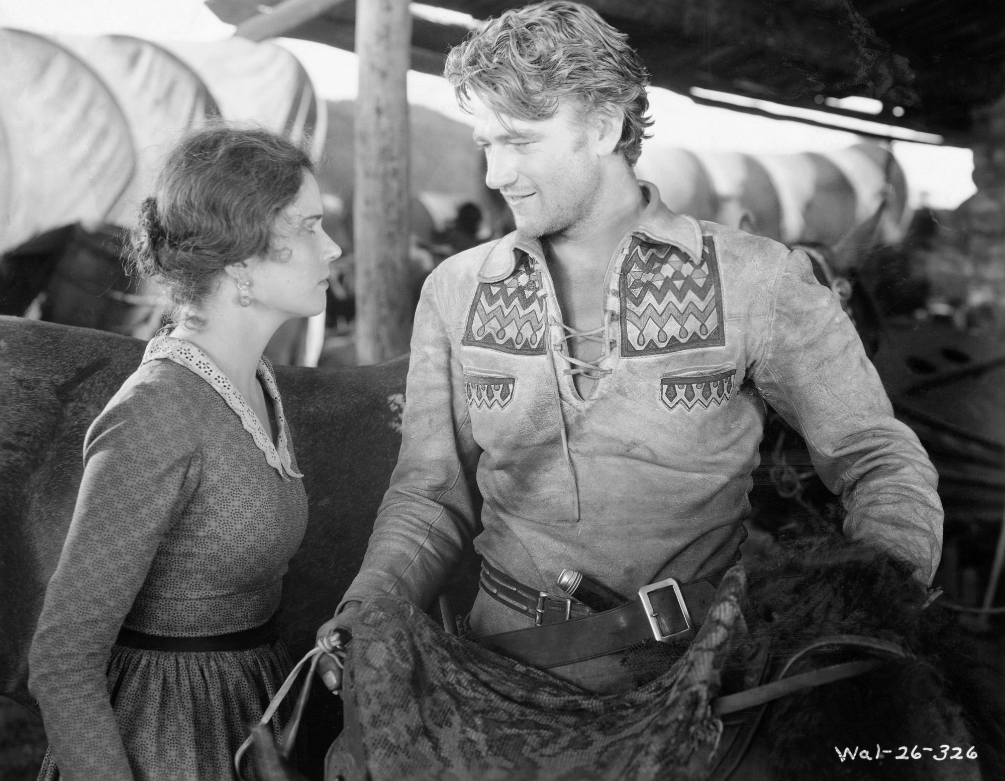 John Wayne as Breck Coleman and Marguerite Churchill as Ruth Cameron in one of his first movies 'The Big Trail' looking at each other with a horse behind them