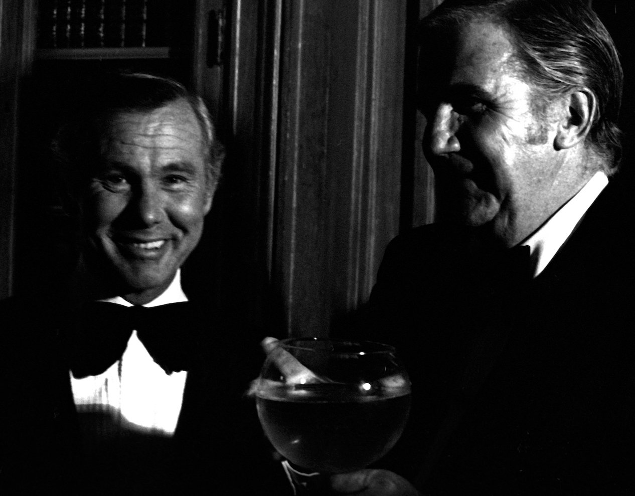 Black and white photo of Johnny Carson and Ed McMahon in tuxedos. McMahon is holding a large wine glass.