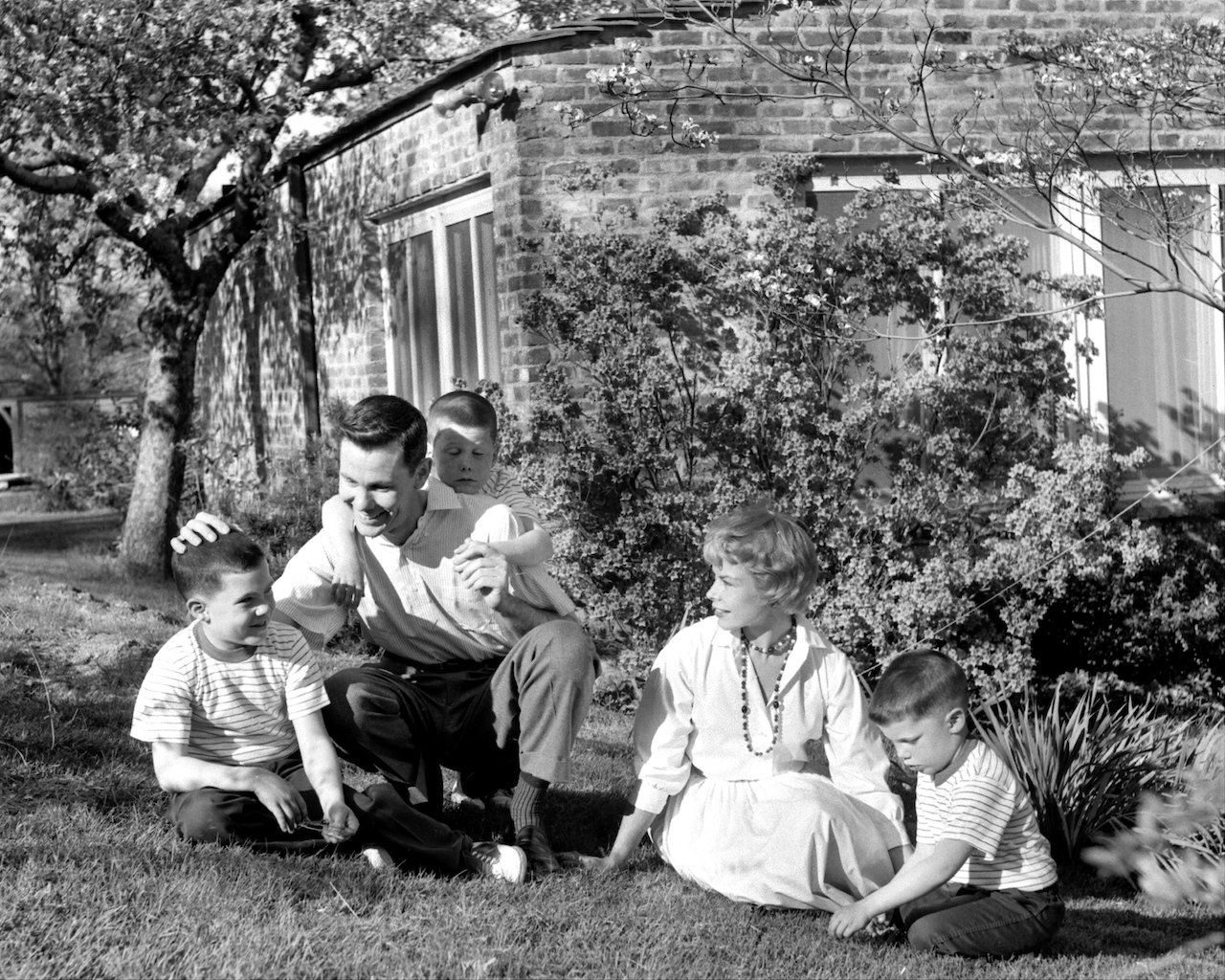 Black and white photo of Johnny Carson and his wife, Jody, on the lawn of their home, playing with their three young kids c. 1958