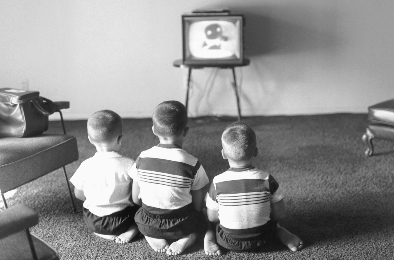 Black and white photo of Cory, Christopher, and Richard Carson from behind, sitting on their feet watching TV