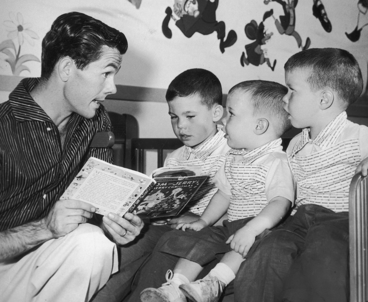 Johnny Carson kneels while he reads a children's book to (L-R): Christopher, Cory and Richard Carson, in their nursery c. 1955