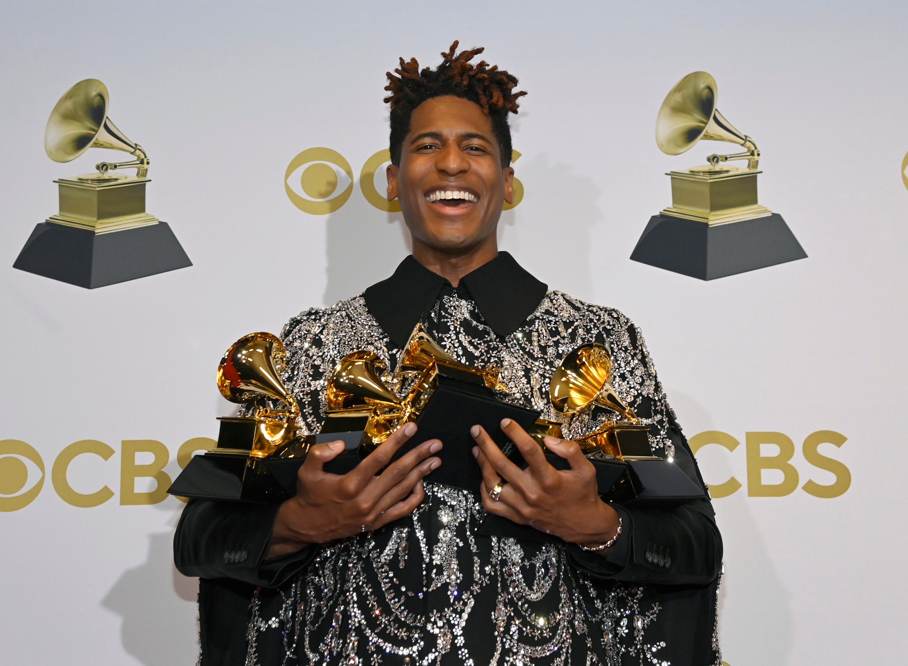 Jon Batiste holds multiple Grammy Award trophies in the winners photo room at the 2022 Grammy Awards