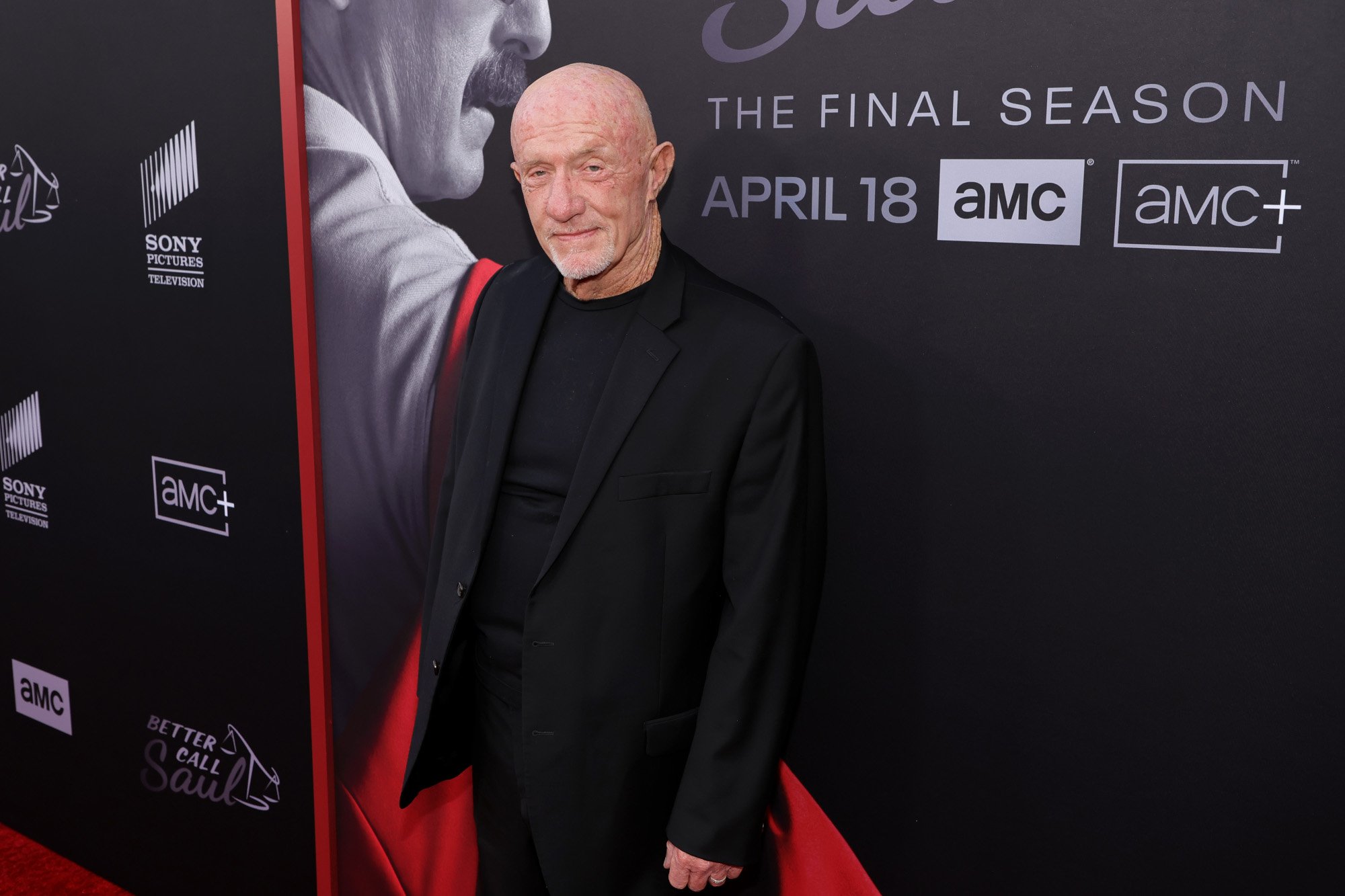 Jonathan Banks on the red carpet for the 'Better Call Saul' premiere. He's wearing a black suit and standing in front of a wall promoting the final season.