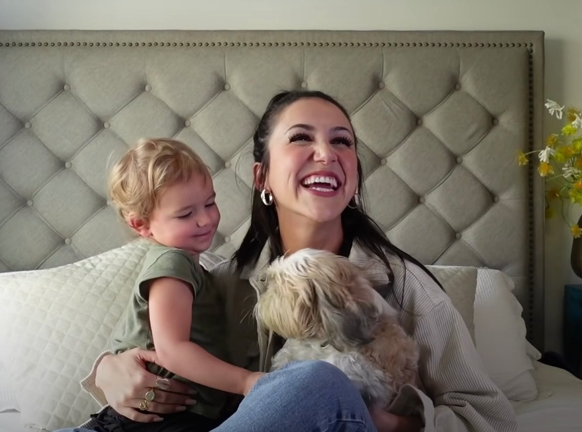 Kat Stickler smiles with her daughter and dog while sitting on her bed