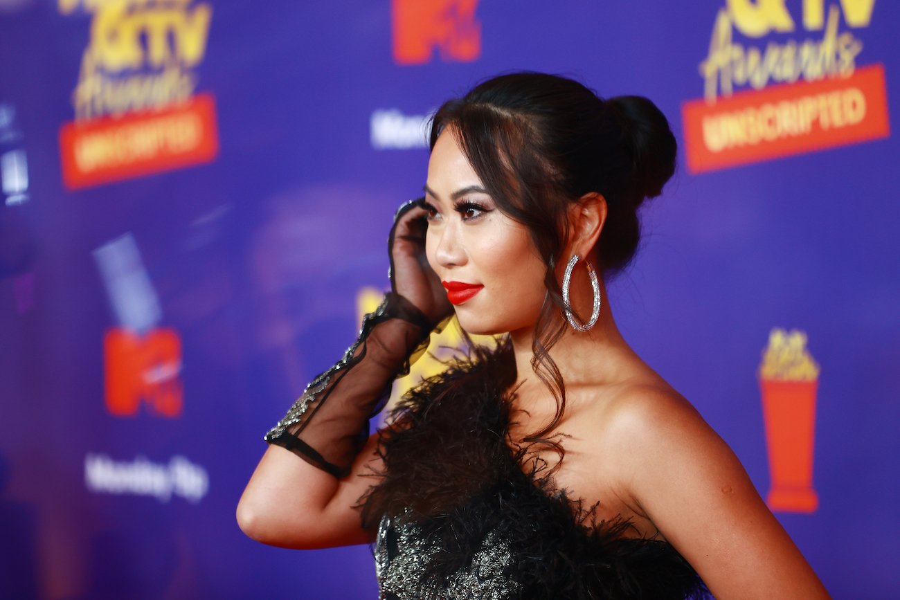 Kelly Mi Li seeing from the side. She is wearing a black outfit in front of a purple background