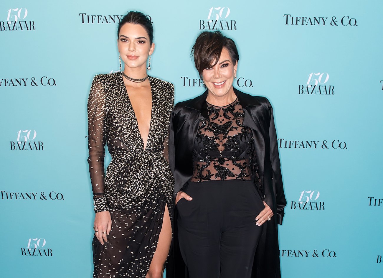 Kendall Jenner and Kris Jenner wearing black outfits and standing in front of a teal background