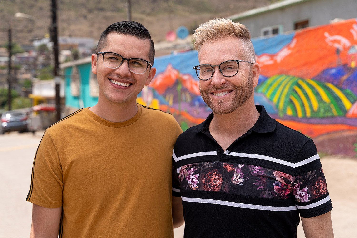 Kenneth 'Kenny' Niedermeier and Armando Rubio standing together in front of a colorful mural for promo for '90 Day Fiancé: The Other Way' Season 3.