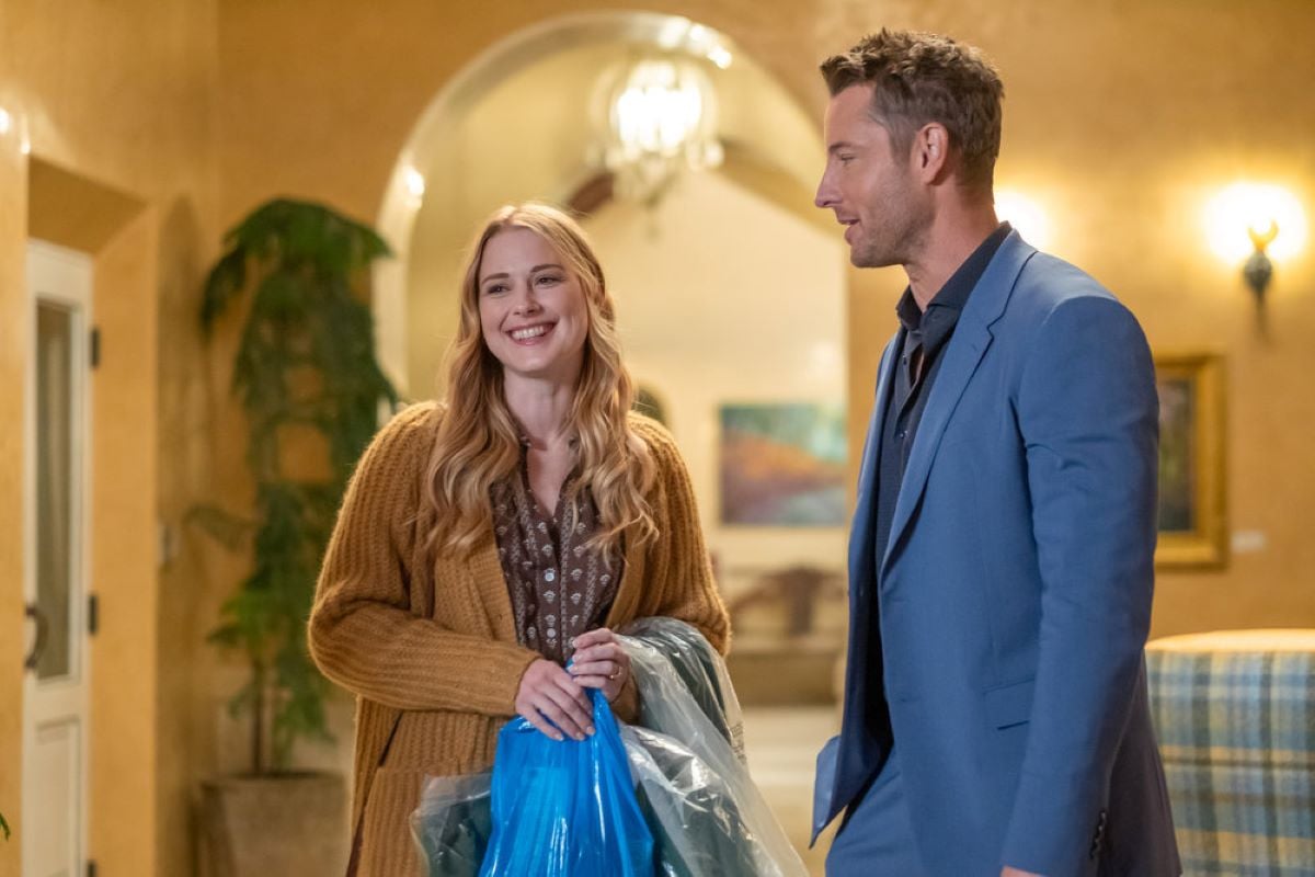 Alexandra Breckenridge and Justin Hartley, who play Sophie and Kevin in 'This Is Us' Season 6 Episode 14, share a scene. Sophie wears a light brown/yellow cardigan over a brown and white blouse. Kevin wears a light blue suit over a dark blue button-up shirt.