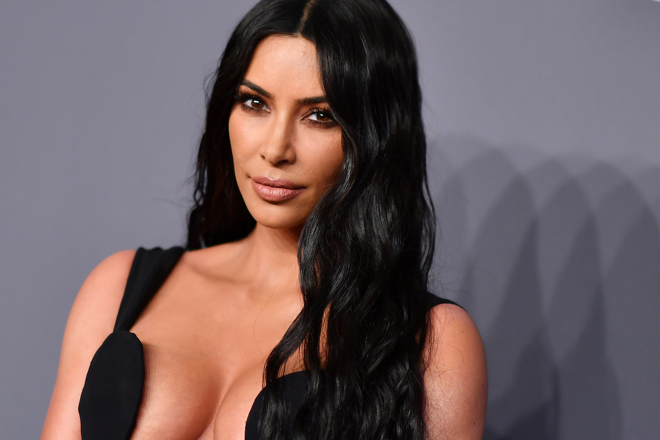 Kim Kardashian wearing a low-cut black outfit and looking on in front of a gray background
